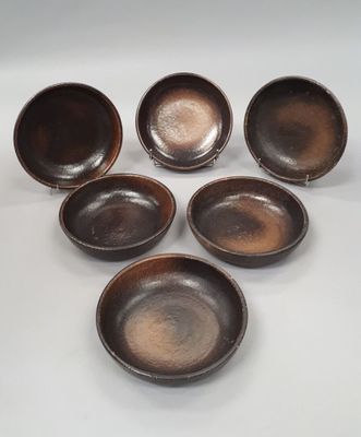 six brown bowls are arranged in a circle on a white surface