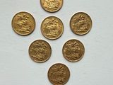 six gold sovereigns are arranged in a triangle on a white surface
