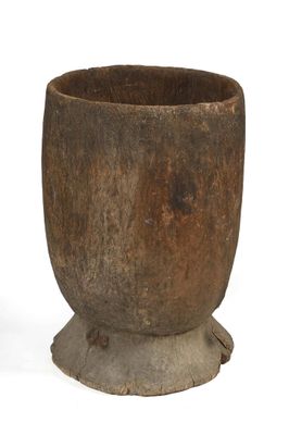 une vieille tasse en bois posée sur un socle, sur une surface blanche