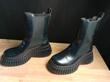 une paire de bottes noires posées sur une table en bois, avec un mur noir en arrière-plan