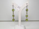 une paire de boucles d'oreilles en péridot et diamants, exposée sur un présentoir blanc