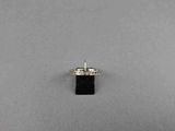 un gros plan d'une bague sertie d'un diamant et d'une pierre noire sur une surface grise