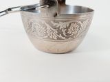 a silver bowl with a spoon in it on a white surface