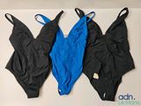 trois maillots de bain noirs et bleus accrochés à un mur blanc