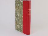 an old book with a red cover sitting on top of a white surface