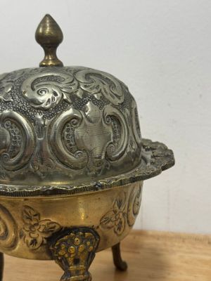 un plat ancien en argent avec un couvercle bombé, posé sur une table en bois