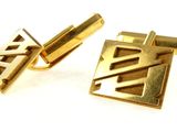 two gold cufflinks on a white surface with a white background