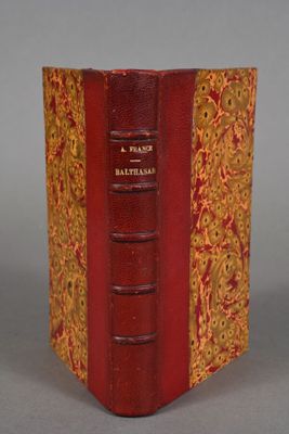 an old book with a red cover sitting on top of a table