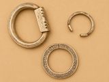 trois bijoux en argent posés sur une surface beige clair