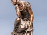 bronze statue of a woman sitting on a rock with her hand on her chin