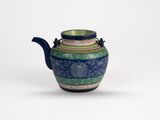 une théière bleue et verte posée sur une surface blanche