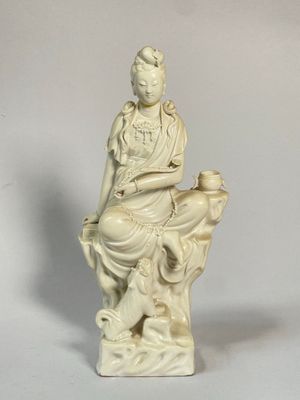 une statue blanche représentant une femme assise sur un rocher