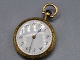 une montre de poche en or avec un cadran blanc sur un fond gris