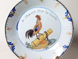 une assiette ornée d'un coq, posée sur un socle