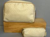 beige ostrich cosmetic bag and pencil case on wooden stand