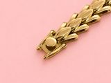 an image of a gold bracelet on a pink surface