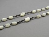 a close up of a long necklace with white beads on a gray surface