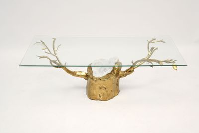 a glass table with a gold base and a tree branch on it