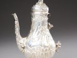 a silver tea pot and a silver spoon on a table