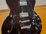 a black guitar sitting on a wooden floor in front of a white wall