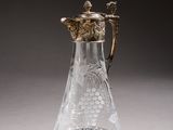 a glass pitcher with a gold handle on a table