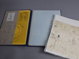 two notebooks with drawings on them sitting on top of a table