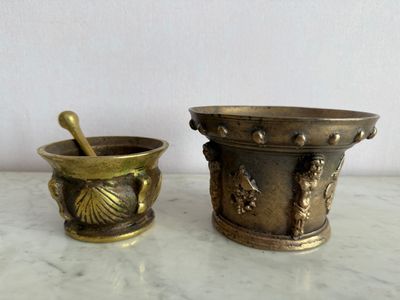 un ensemble composé d'un mortier et de brosses à mortier anciens en laiton, posés sur une table en marbre