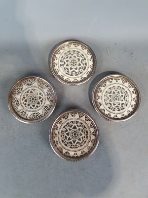 quatre sous-verres en argent ornés de motifs complexes, posés sur une table