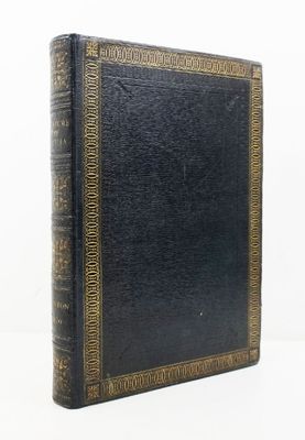 un vieux livre noir aux tranches dorées posé sur une surface blanche