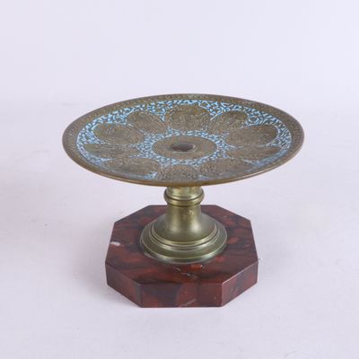 une plaque en laiton ornée d'un motif bleu, posée sur un socle en bois