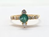 a close up of a green emerald and diamond ring on a white surface