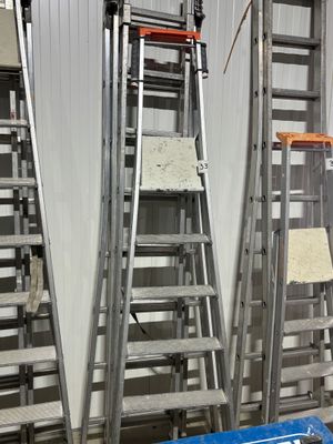 several ladders are lined up in a warehouse with a sign on the floor