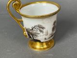 a close up of a cup with a gold handle on a table