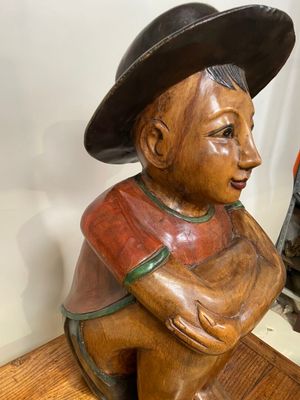 une statue en bois représentant un garçon coiffé d'un chapeau