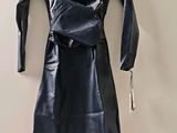 une robe en cuir noir suspendue à un cintre devant un mur blanc