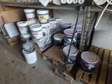 several buckets of paint are stacked on pallets in a garage
