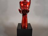sculpture of a red hand holding a red apple on a black base