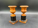 une paire de vases orange et noirs posés sur des socles en bois, sur une table