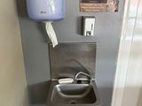 un lavabo en acier inoxydable dans des toilettes publiques, avec un sèche-mains bleu fixé au mur