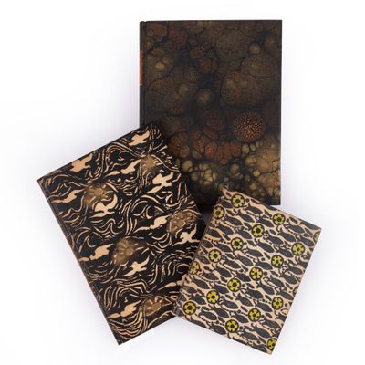 trois cahiers aux motifs variés posés sur une surface blanche