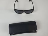 une paire de lunettes de soleil noires et un étui noir posés sur une surface blanche