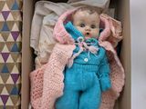 a small doll in a box with a blanket on it
