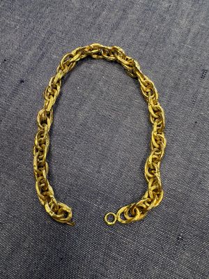 un gros plan d'un bracelet à maillons dorés posé sur un tissu gris
