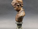 a bronze bust of a man with a hat on top of a pedestal
