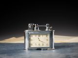une petite horloge en argent posée sur une table, avec un livre en arrière-plan