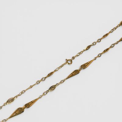 un collier plaqué or composé d'une longue chaîne posée sur un fond blanc