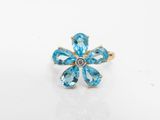 une photo d'une bague ornée d'une fleur en topaze bleue, posée sur une surface blanche