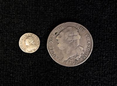 an old silver coin and a silver coin on a black surface