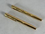 two gold colored pens sitting next to each other on a piece of paper