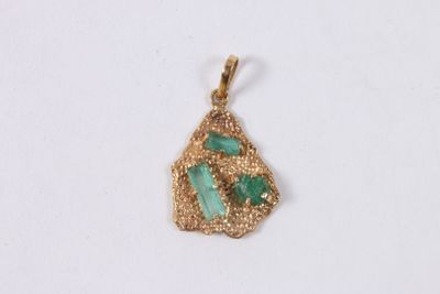 un gros plan d'un pendentif doré et vert sur une surface blanche